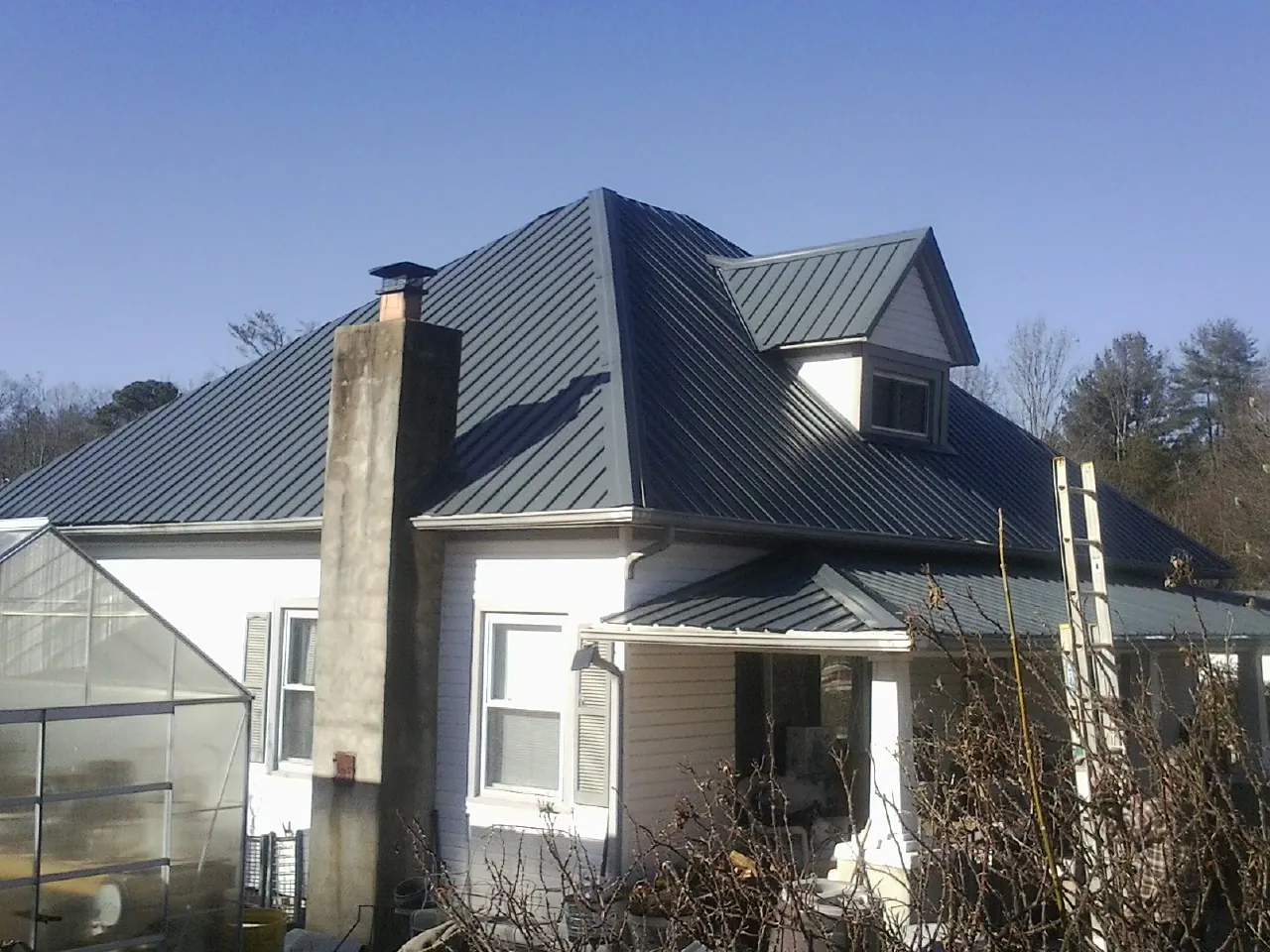 Dark blue standing seam metal roof on a white farmhouse with dormer — Slate & Tile Roof Repair by Roofing Brothers in Danese