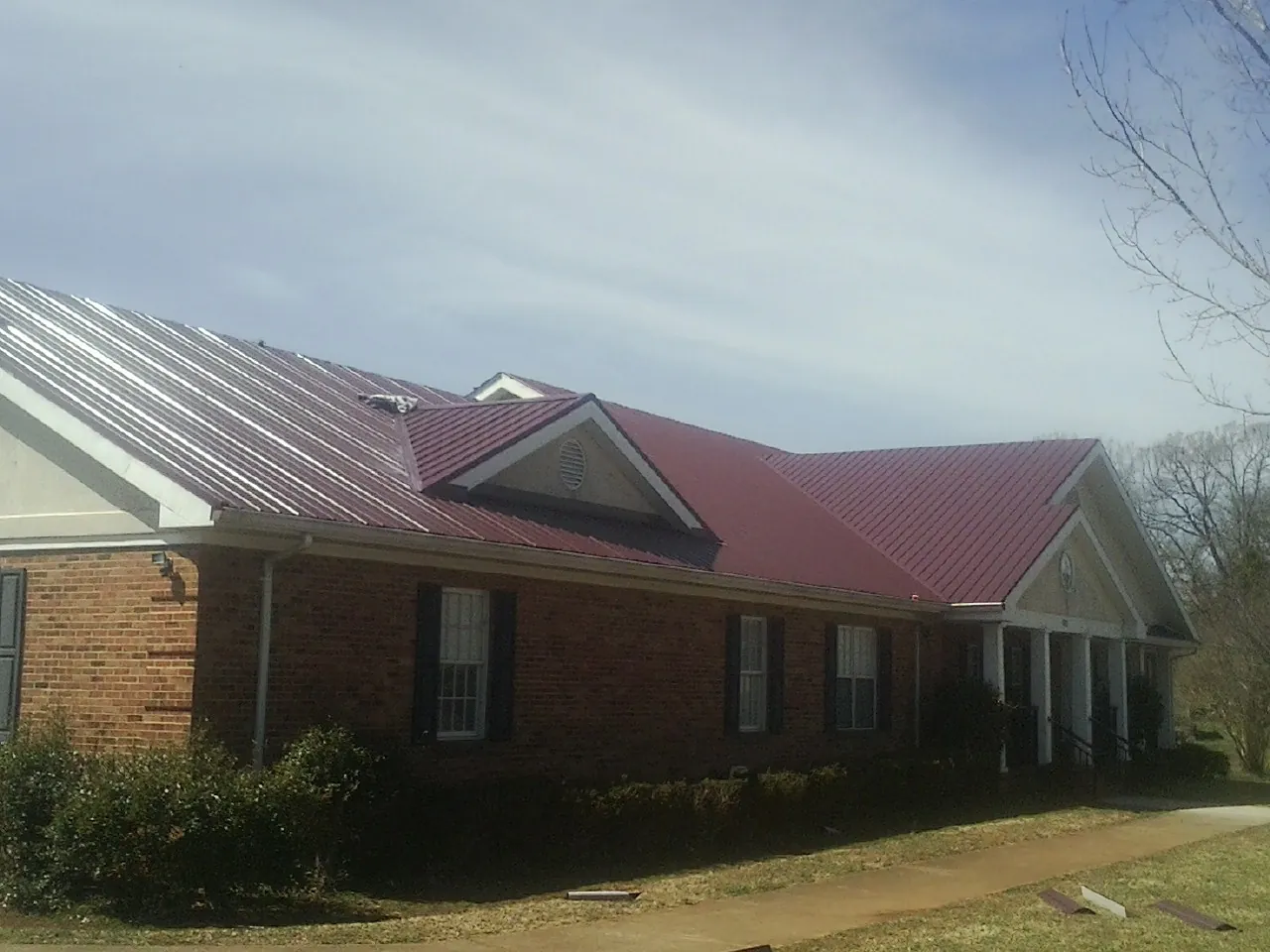 Red metal roof with gabled entries on a long brick building, from a Hail Damage Roof Repair job in Danese