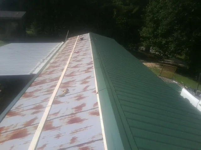 Old rusted panels beside newly installed green metal roofing — Wind Damage Roof Repair by Roofing Brothers in Danese
