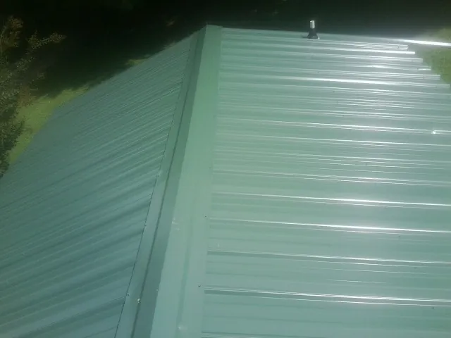 New green metal panels meeting at the ridge of a roof — Flat Roof Repair work by our crew in Danese