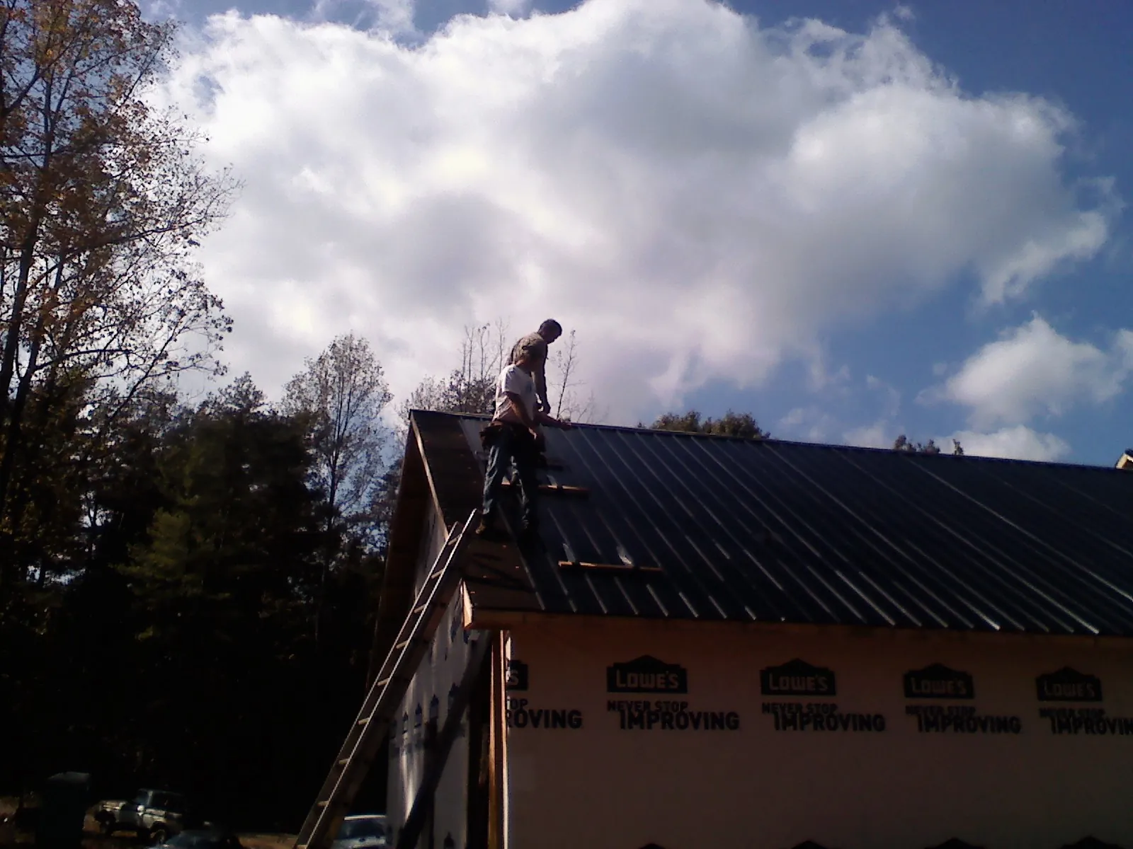 Roofer fastening dark metal panels high against a cloudy sky, from a Roof Inspection job in Danese