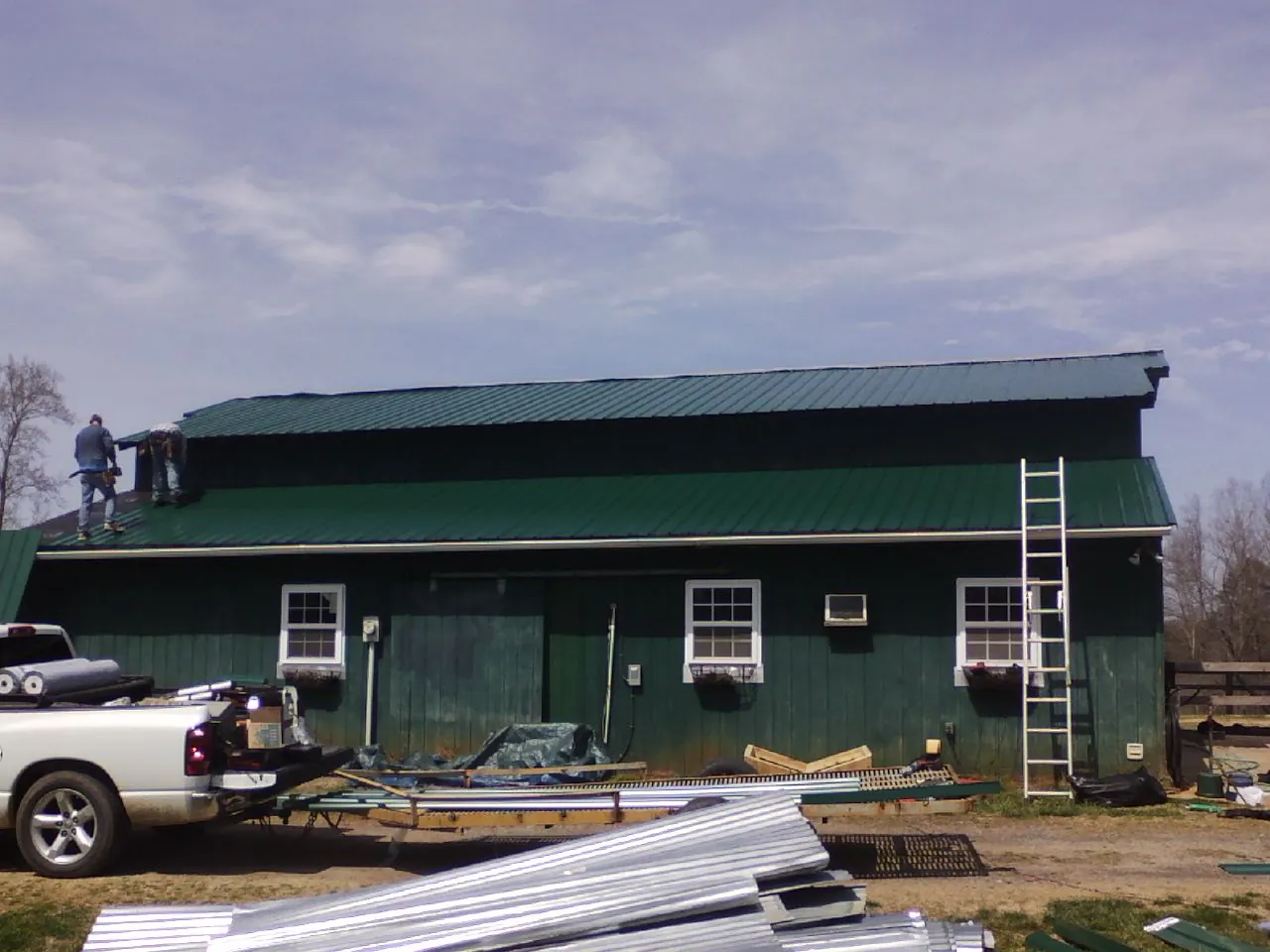 Crew installing green metal roofing on a large green barn in Danese